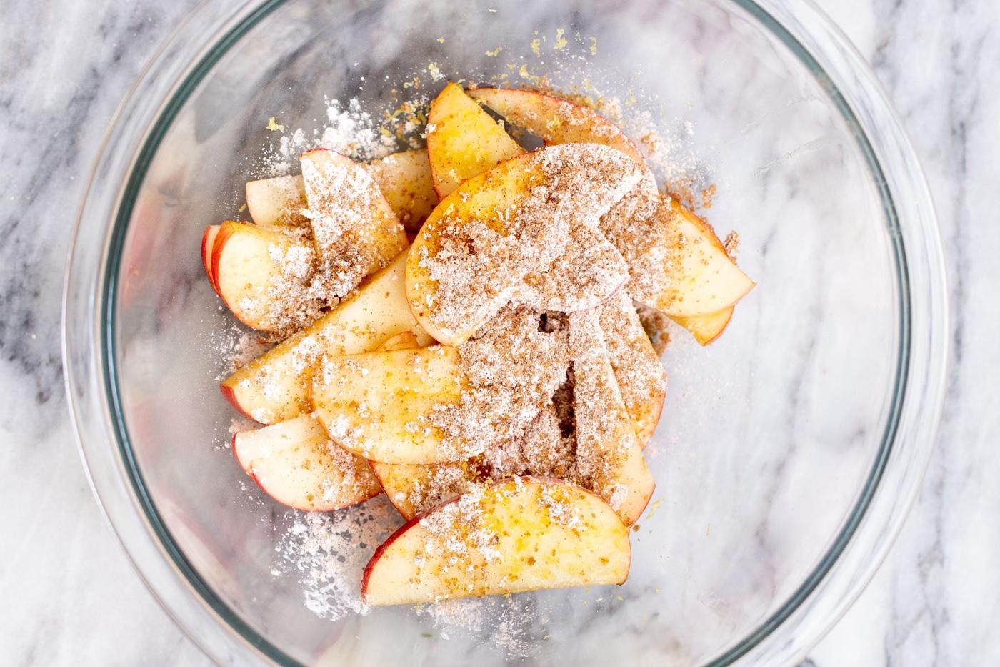 apple slices in a glass bowl being mixed with brown sugar and cornstarch