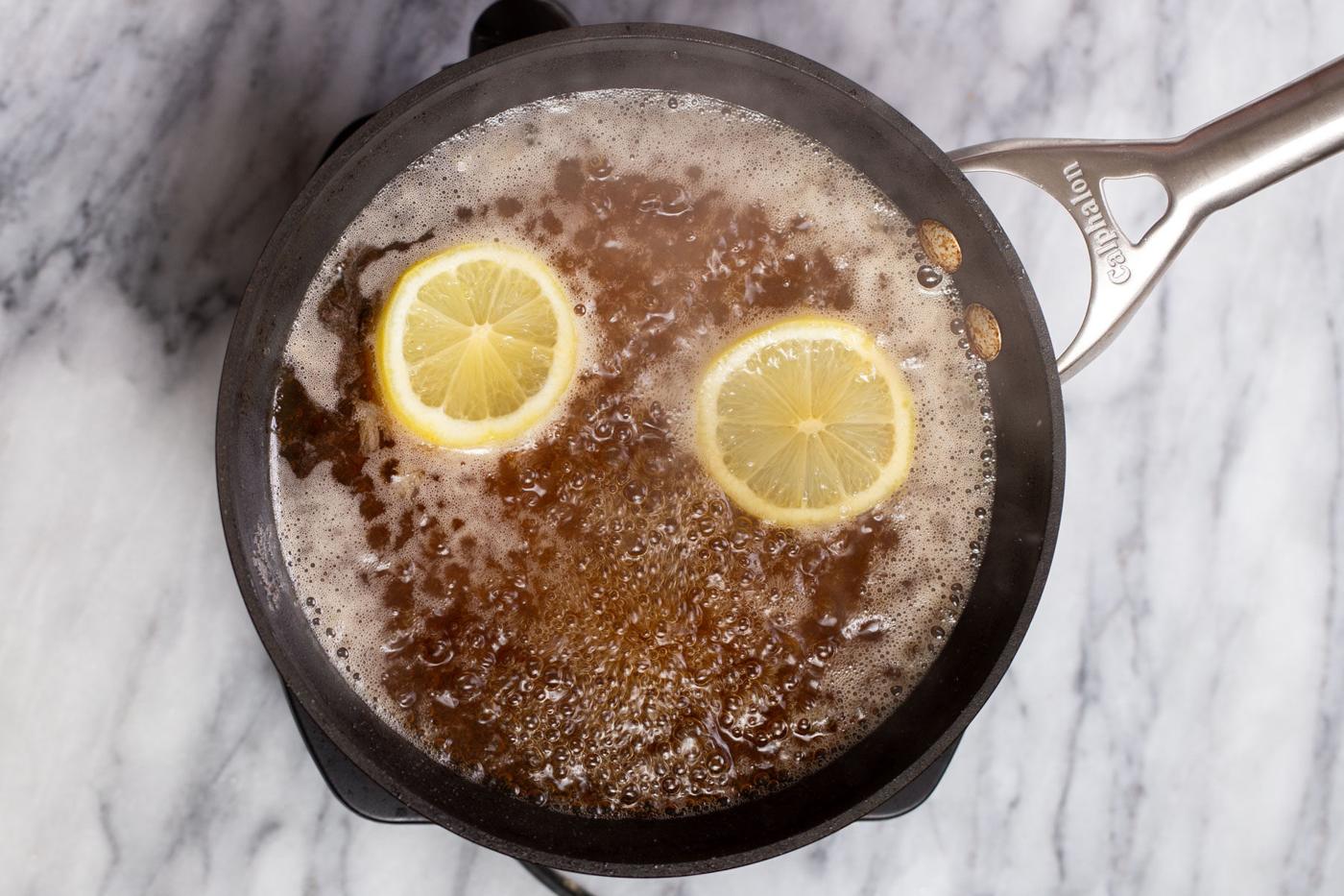 lemon slices being added to bubbling soaking syrup in a saucepan