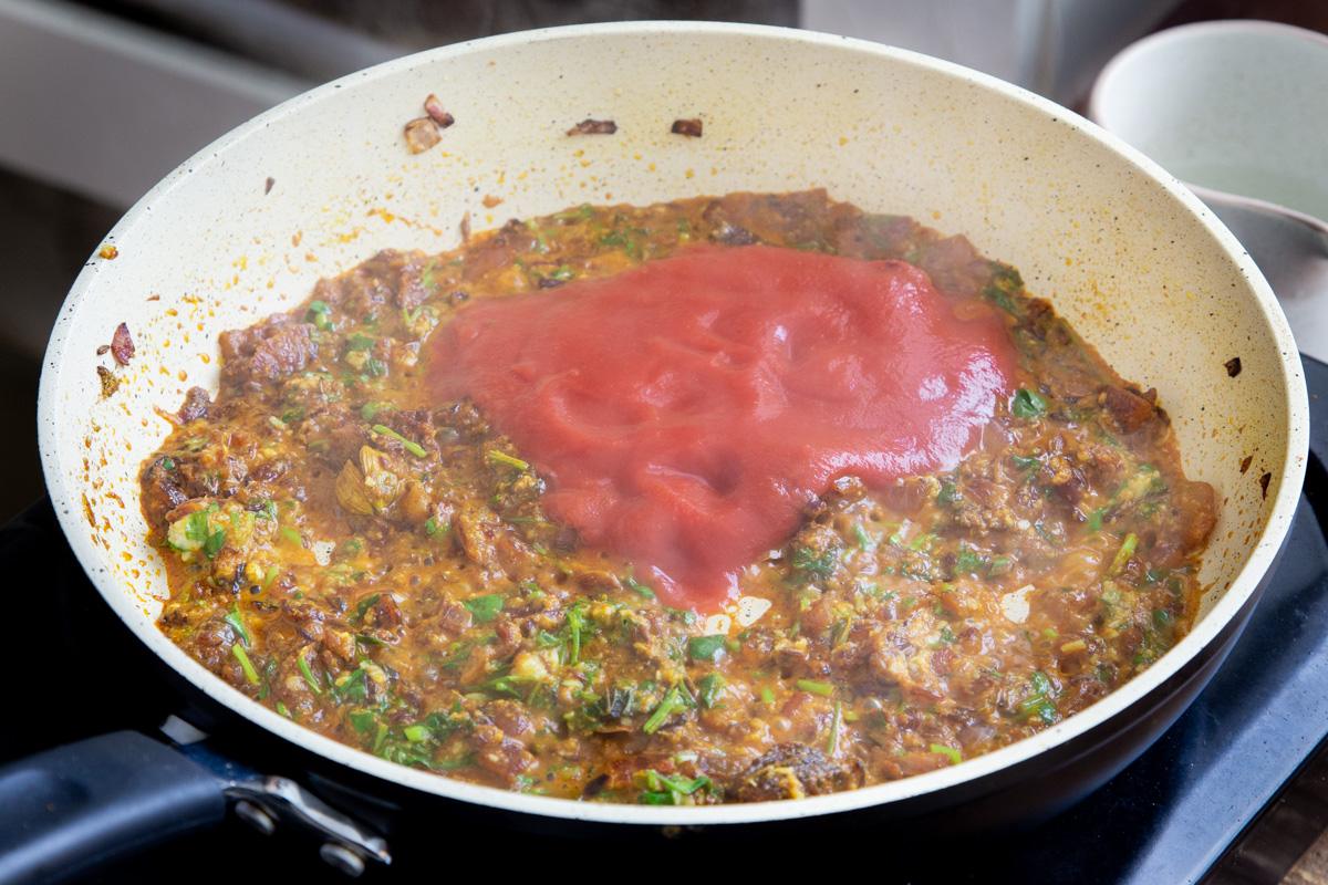 a sauteeing pan with chopped onion, tomato puree and cilantro