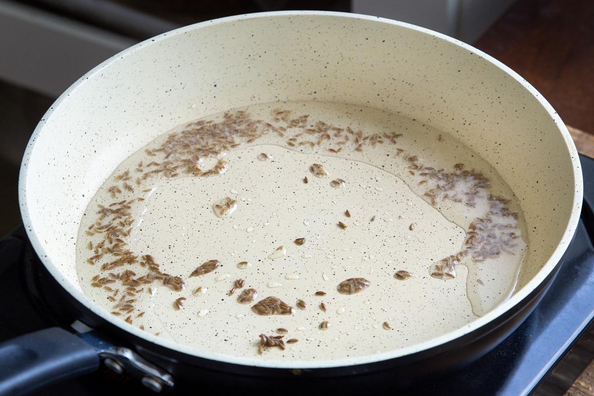 a sauteeing pan with cumin seeds tempering in oil