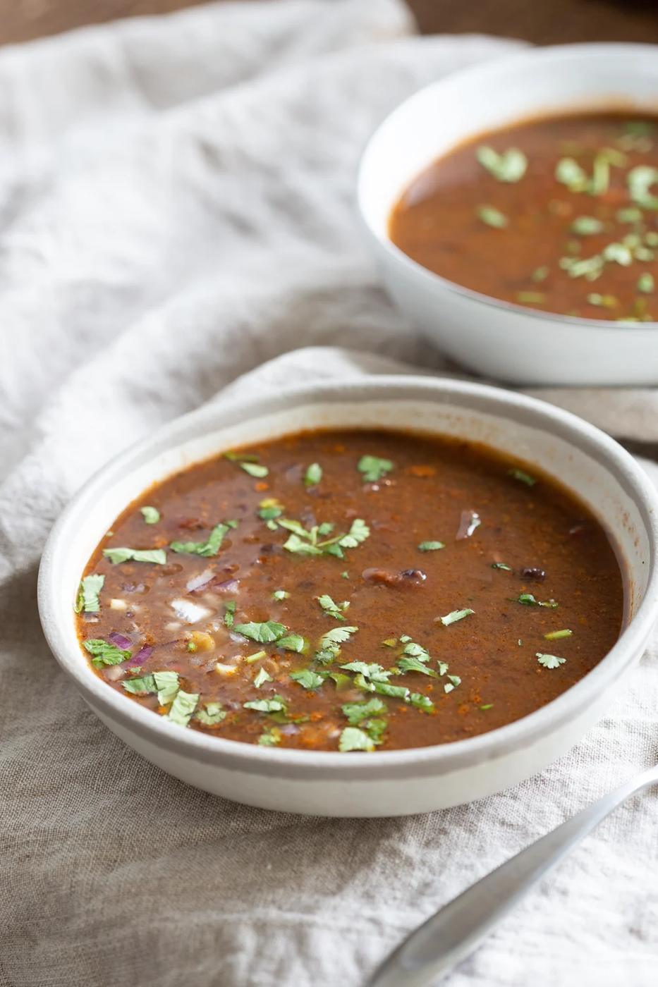 side view of a bowl of vegan Instant Pot black bean soup on a white cloth napkin