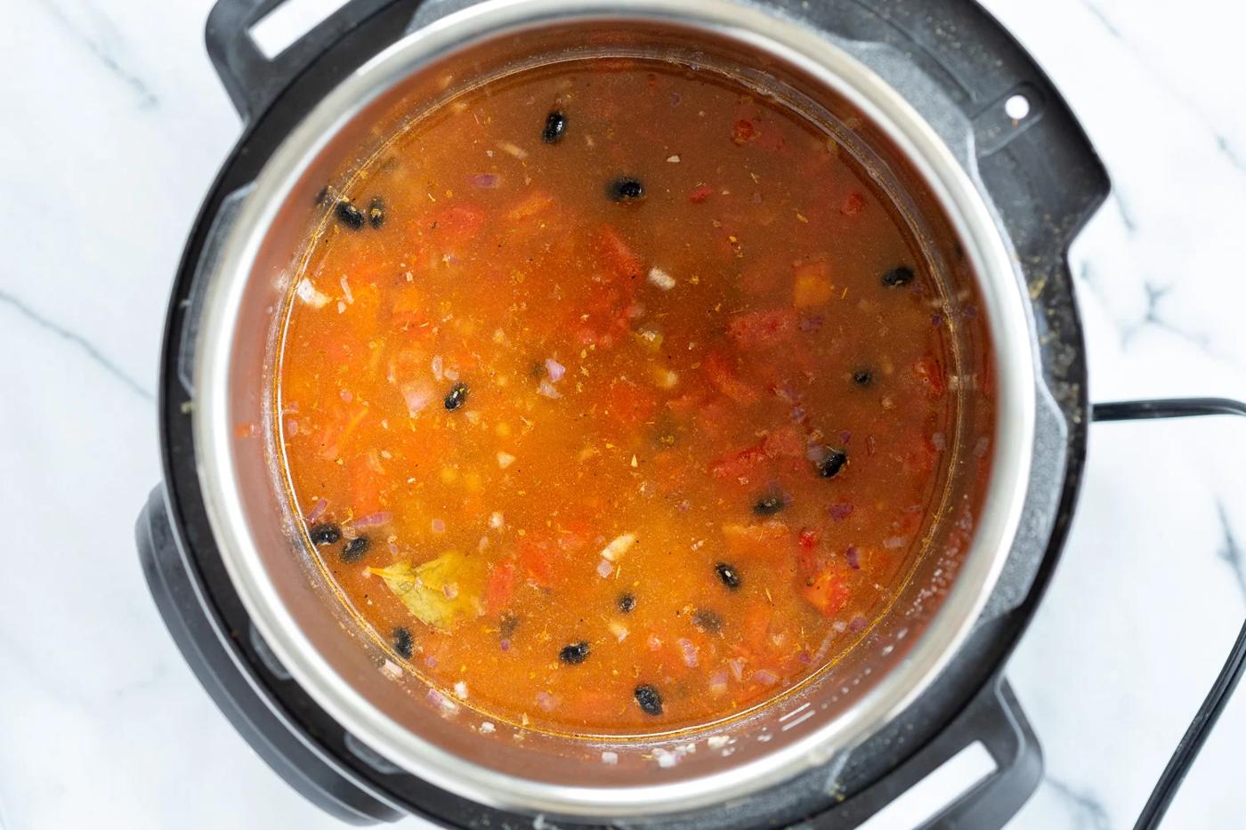 dried soaked beans being added to an Instant Pot filled with seasoned tomato broth