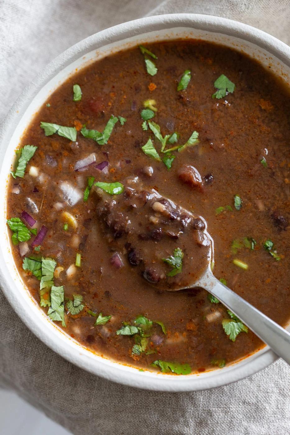 overhead shot of a white bowl with vegan black bean soup with a spoon dipping into the bowl