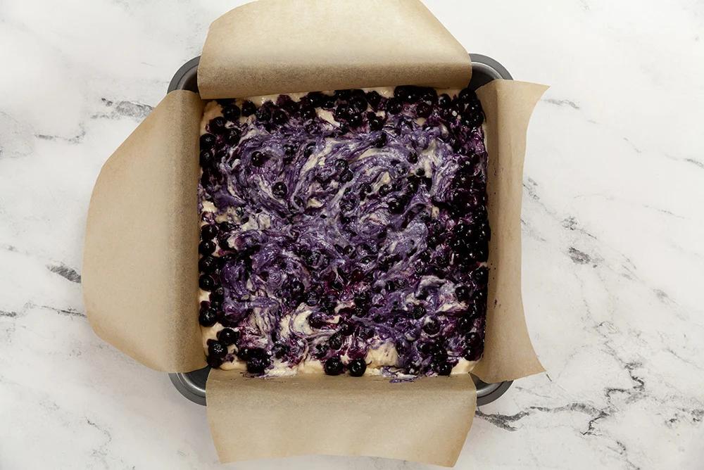 Berry Buckle Batter with blueberries in a parchment lined baking dish