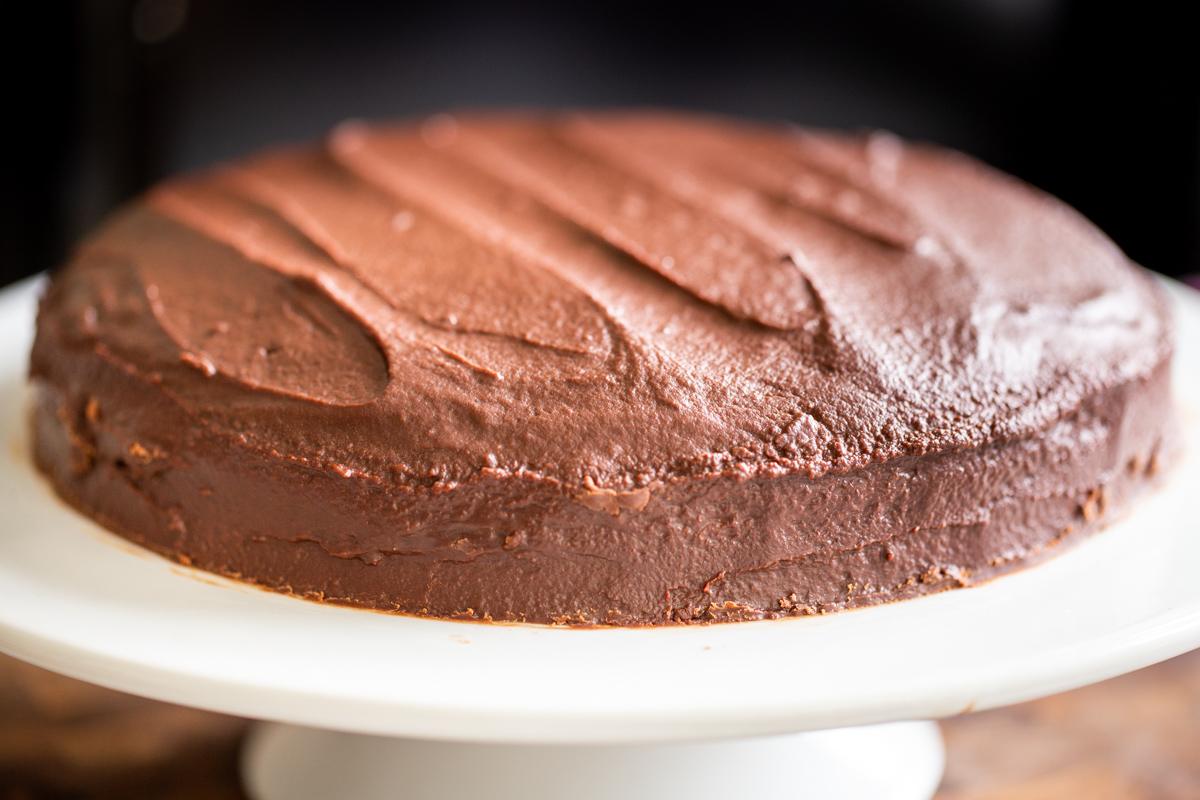 top layer of vegan boston cream pie cake being topped with chocolate ganache