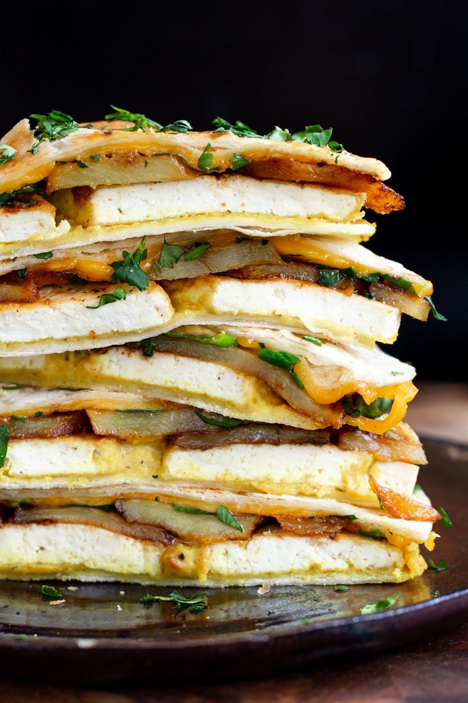 stacked sliced vegan breakfast quesadilla with tofu, potatoes, hummus and vegan cheese