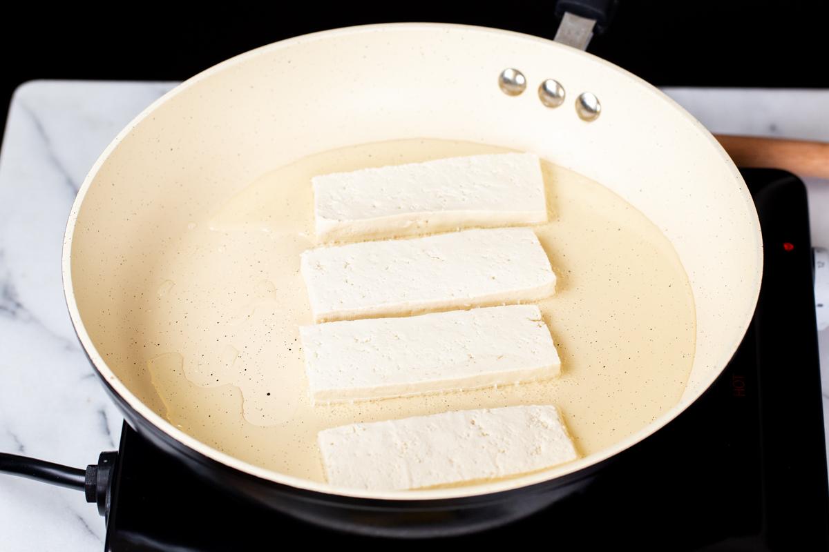 tofu wedged being added to a pan with oil