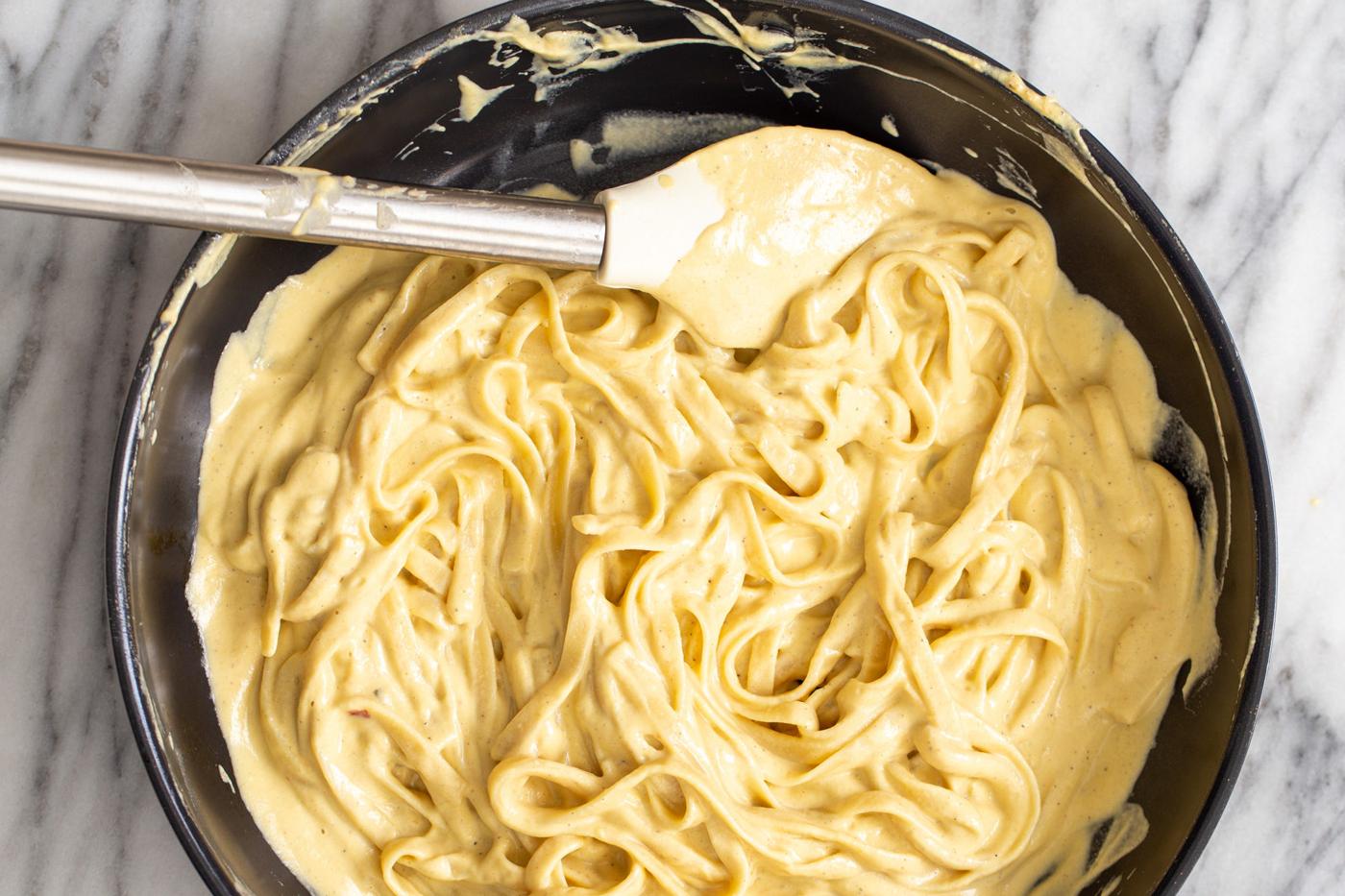 fettuccine being tossed in vegan butternut squash cashew cheese carbonara sauce