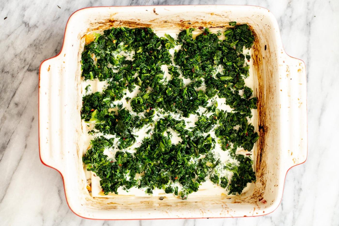 thawed spinach being added on top of lasagna noodles to make vegan butternut squash lasagna