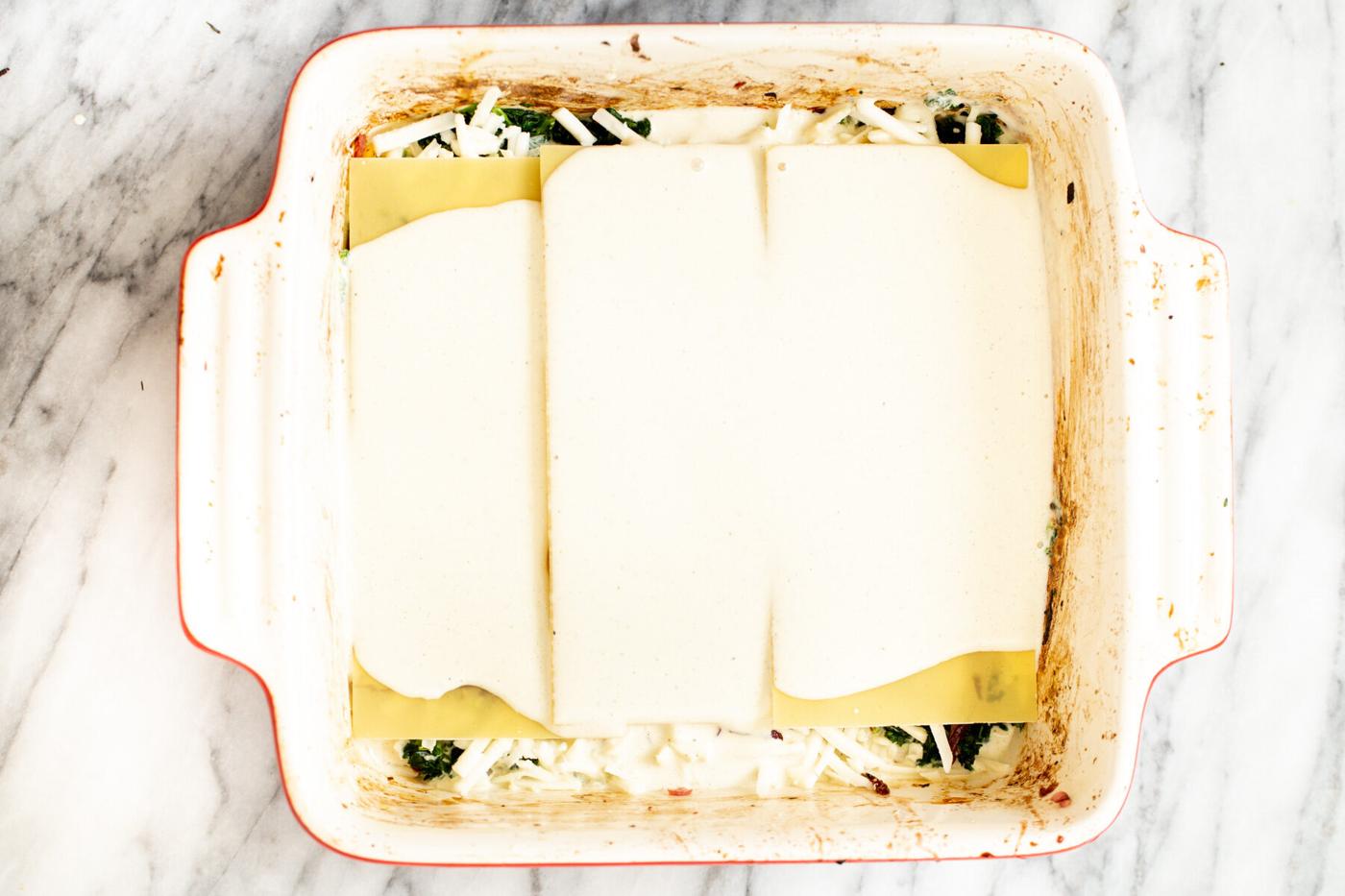 tofu bechamel sauce poured over lasagna sheets in casserole dish to make vegan lasagna recipe