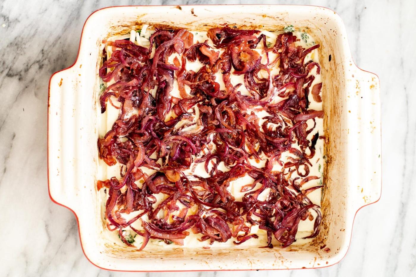 onions and pasta layered in a casserole dish to make vegan lasagna