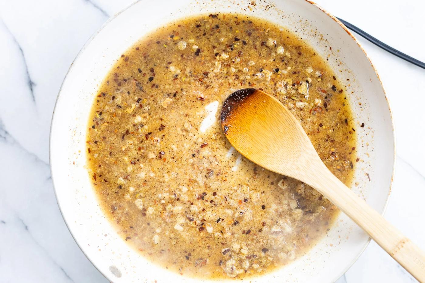 Pepper, vegan parmesan and broth for our vegan cacio e pepe in a white skillet