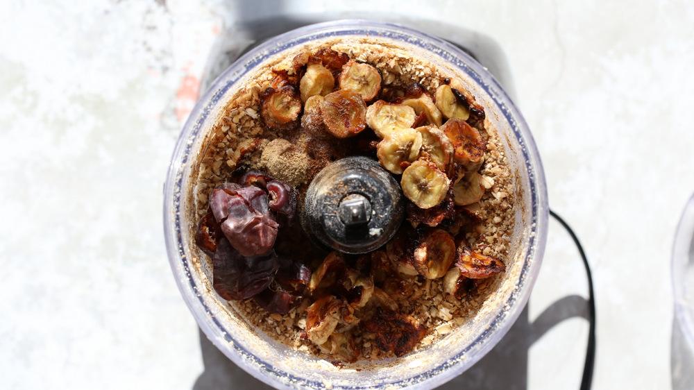 dates and bananas being added to oats and nuts in the container of a food processor