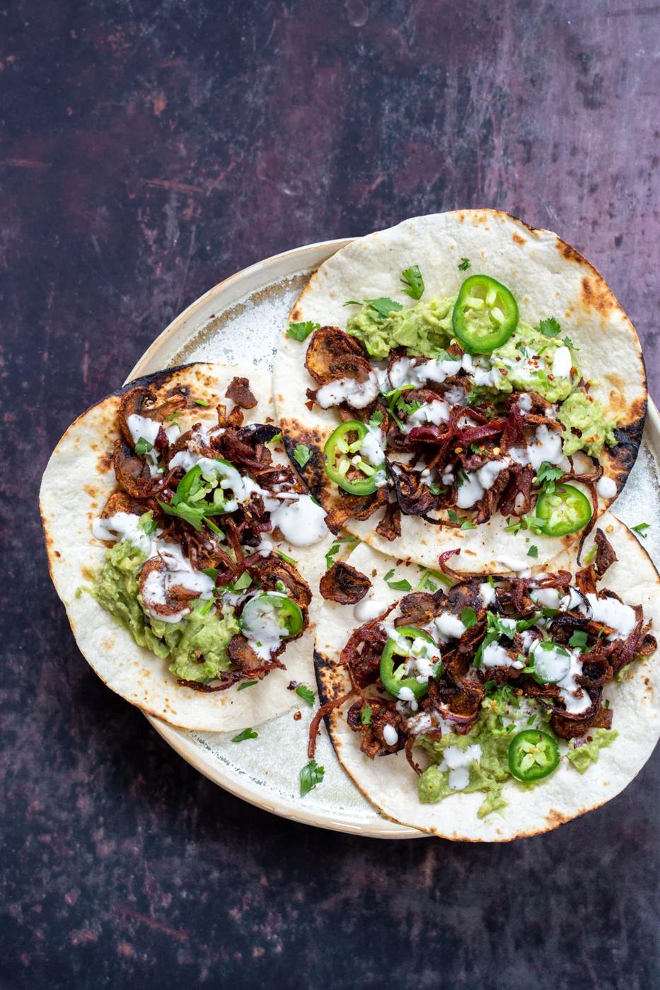 Vegan Carnitas Tacos with mushrooms, guacamole and sour cream placed in a speckled plate