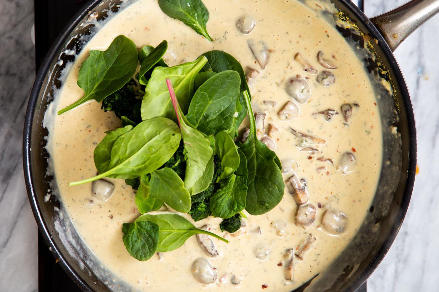 fresh spinach being added to creamy mushroom sauce to make vegan florentine