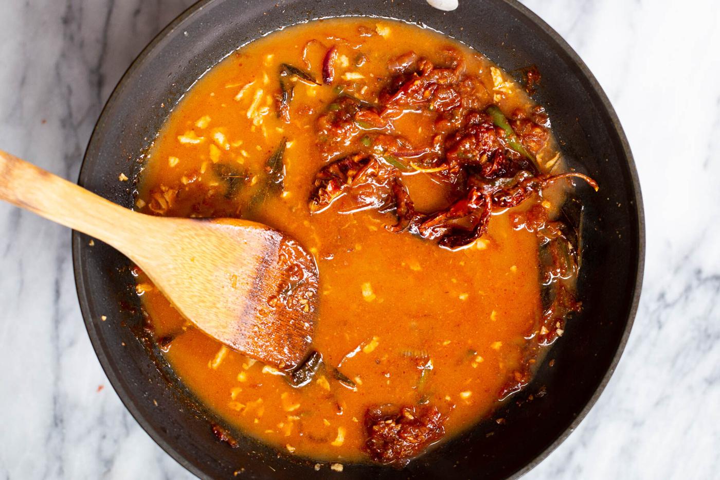 broth being added to thin out chili gravy in a frying pan for chicken kondattam recipe.
