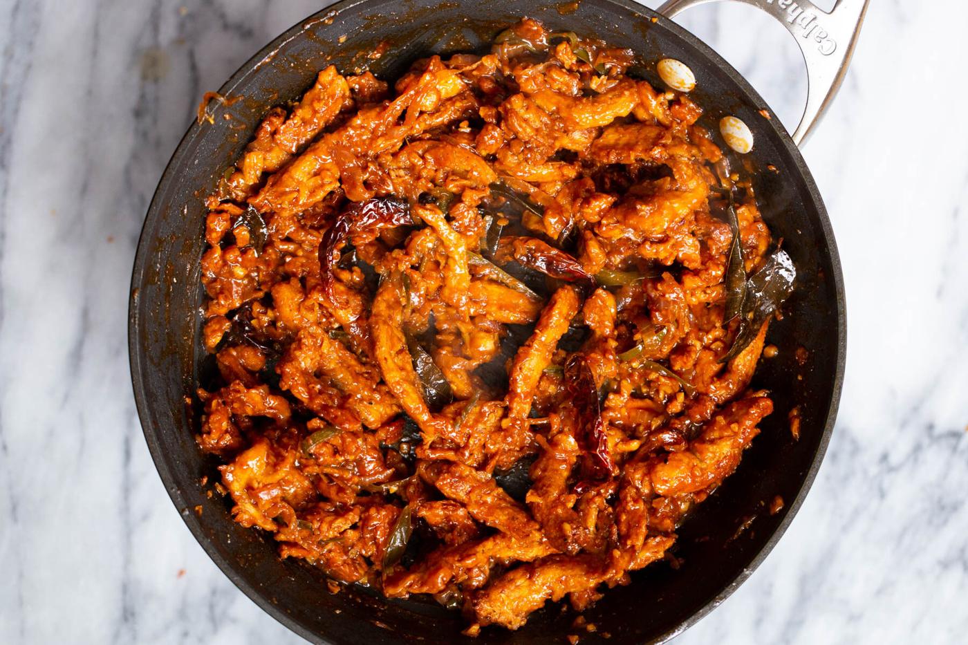 spicy baked soycurls simmering in chili marinade in a black sauteeing pan