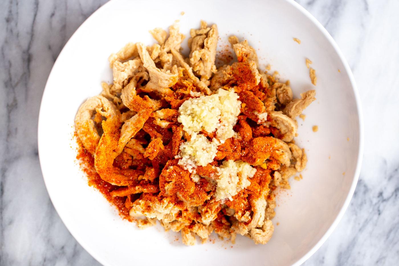 soaked soycurls being mixed with spices in a white bowl