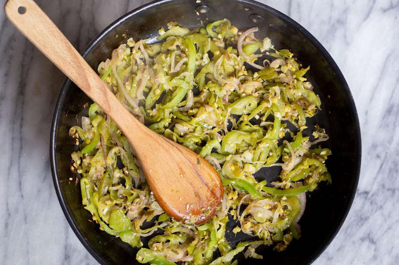 black sauteeing pan with sauteed bell peppers, green chillies, garlic and ginger