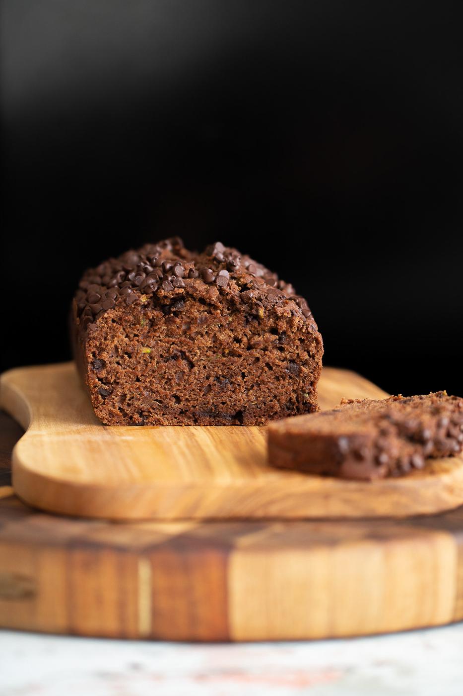a sliced loaf of chocolate zucchini bread on a wooden chopping board