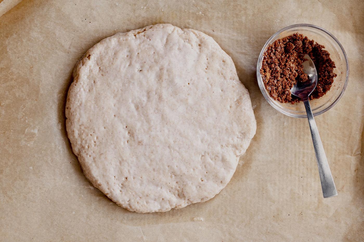 a loaf of vegan biscotti dough on parchment paper before baking and a small bowl with cinnamon sugar