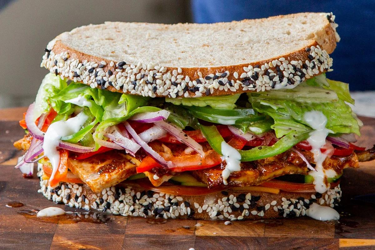 vegan club sandwich with veggies and tofu deli meat on a wooden cutting board