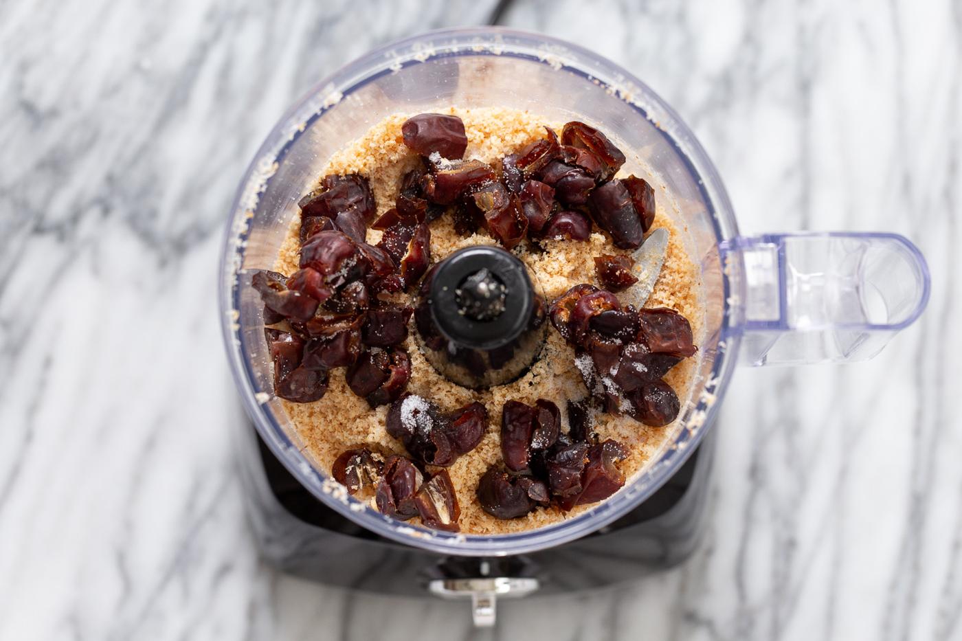 dates being added to toasted coconut in a food processor to make vegan coconut balls