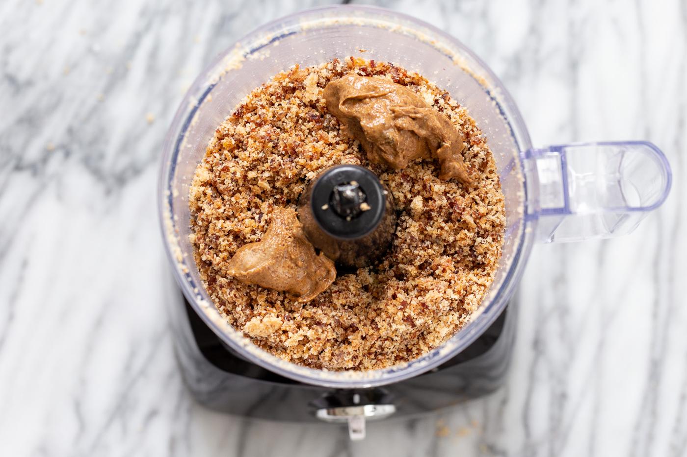 almond butter being added to date and coconut mixture in a food processor to make energy balls