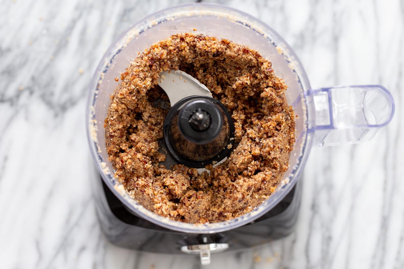 coconut dates and almond butter being blended in a food processor to make vegan energy balls