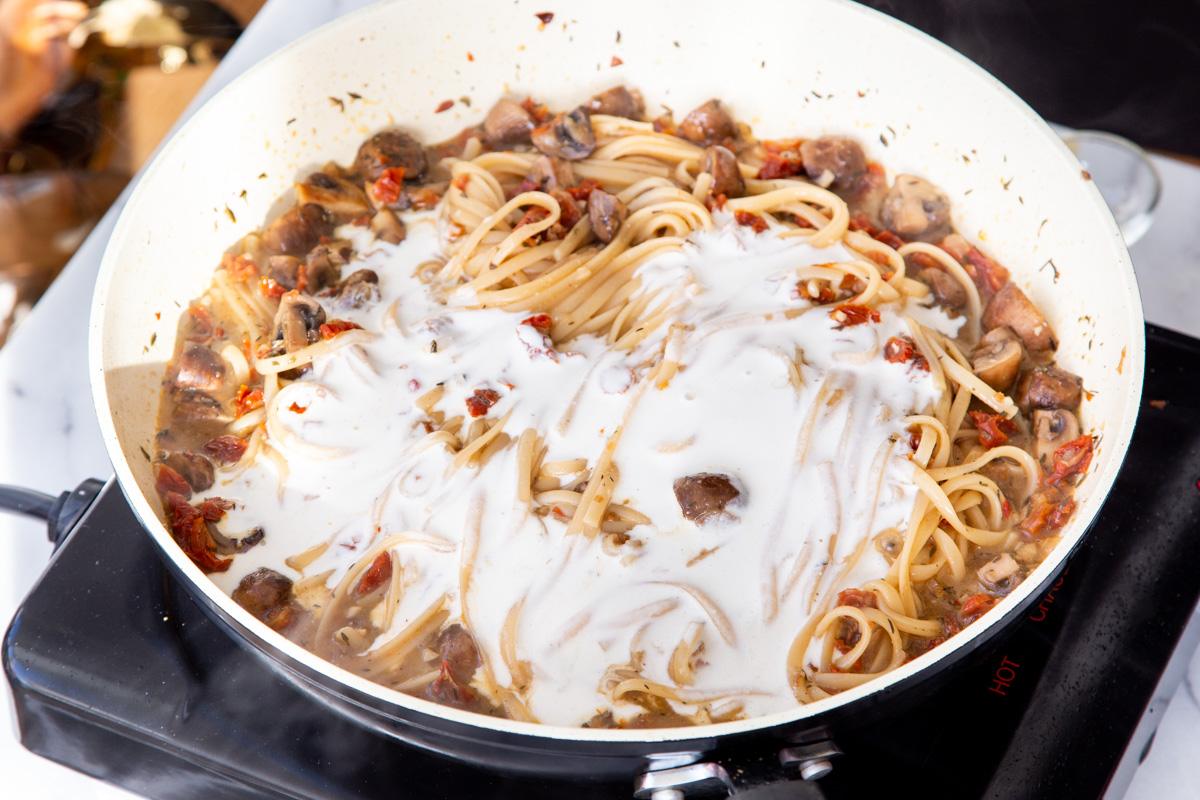 cashew cream being added to one pot mushroom sundried tomato pasta