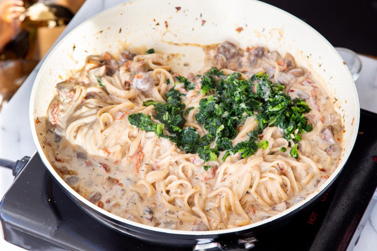 spinach being added to creamy mushroom sundried tomato pasta