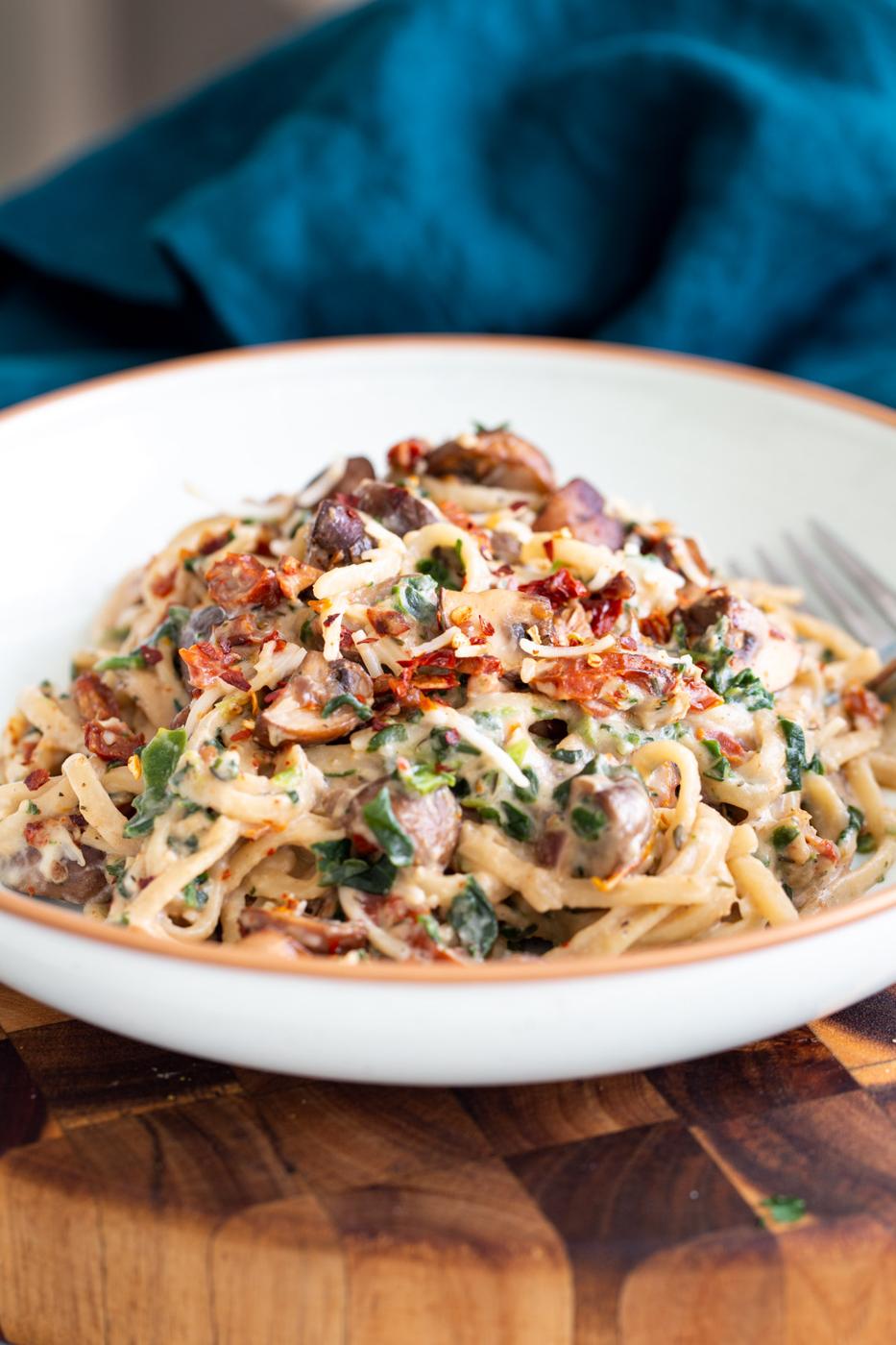 side view of creamy vegan mushroom pasta topped with sundried tomatoes