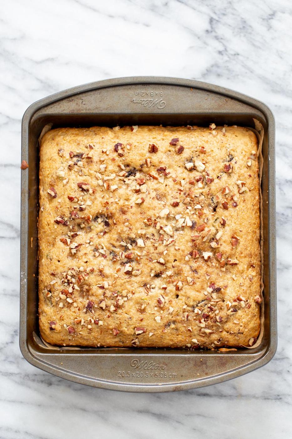 overhead shot of a vegan date nut cake in a cake pan on a marble countertop