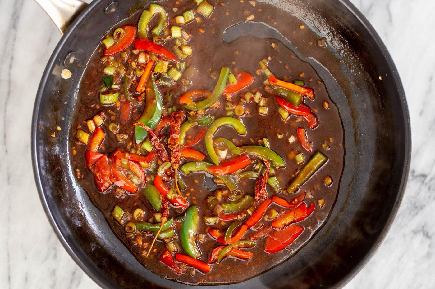chili sauce and soy sauce being added to a frying pan