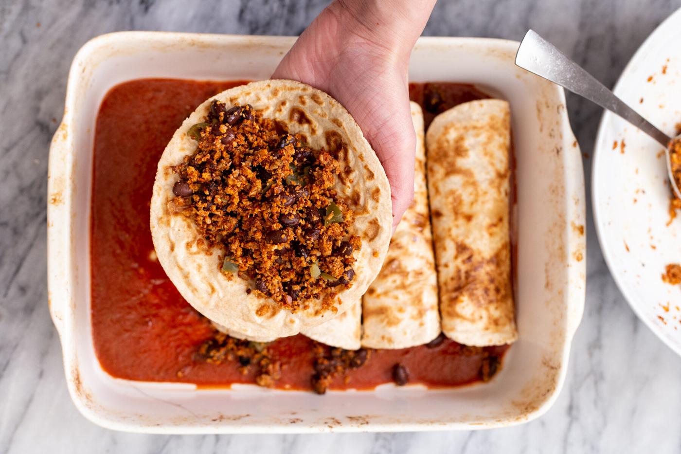 a hand holding a wheat tortilla filled with vegan cauliflower taco meat