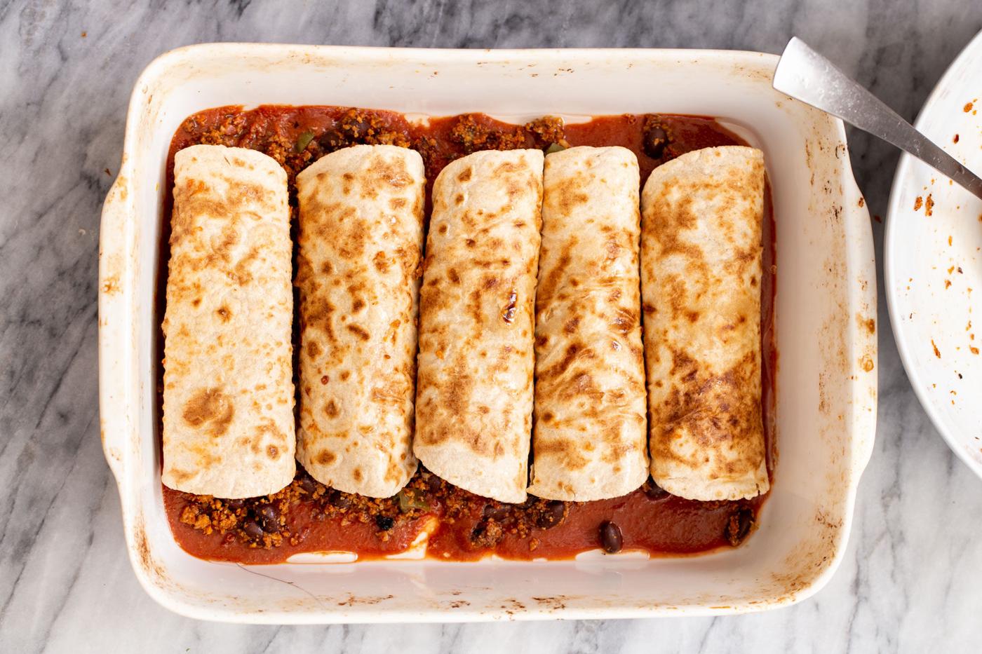 a casserole dish with rolled up enchiladas in tomato sauce