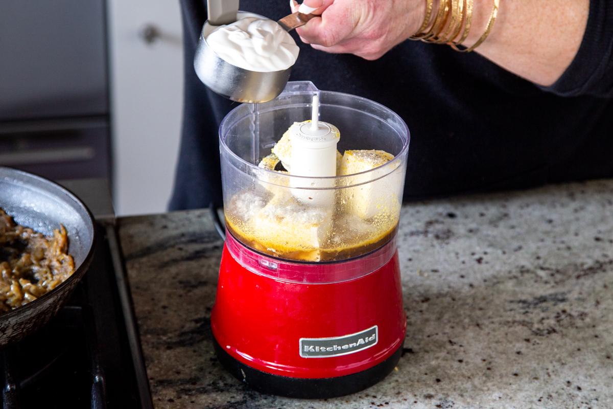 dairy-free yogurt being added to a small food processor with silken tofu and nutritional yeast
