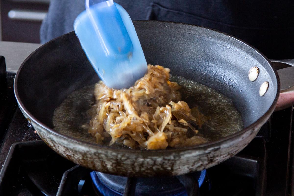 Instant Pot caramelized onions being added to a sauteeing pan to cook down and reduce liquid