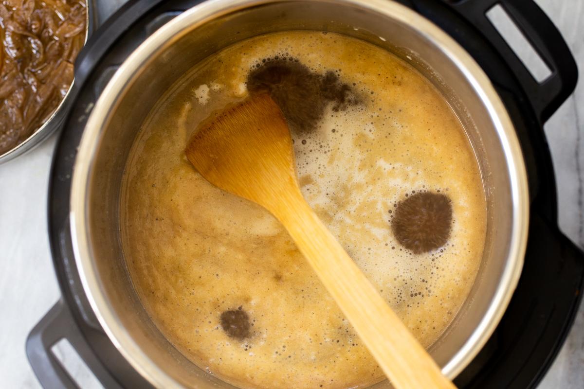 vegan French Onion soup being stirred in an Instant Pot with a wooden spoon