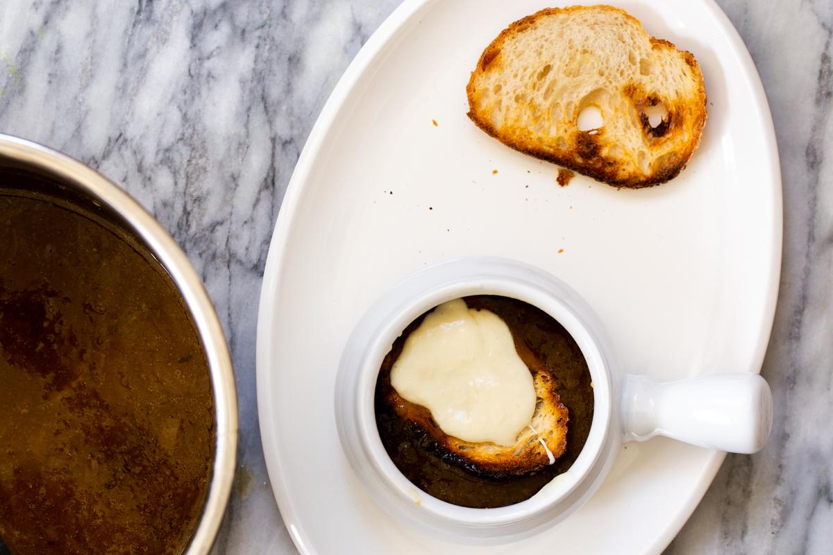 a small serving of vegan French Onion Soup topped with a slice of sourdough topped with liquid mozzarella