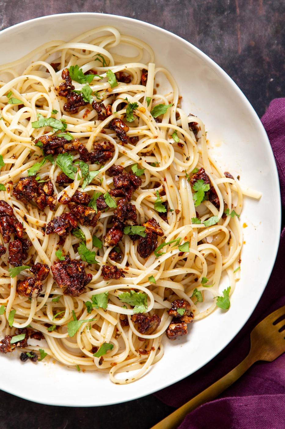 a plate with vegan garlic sun dried tomato chili oil pasta topped with candied pecans and fresh herbs