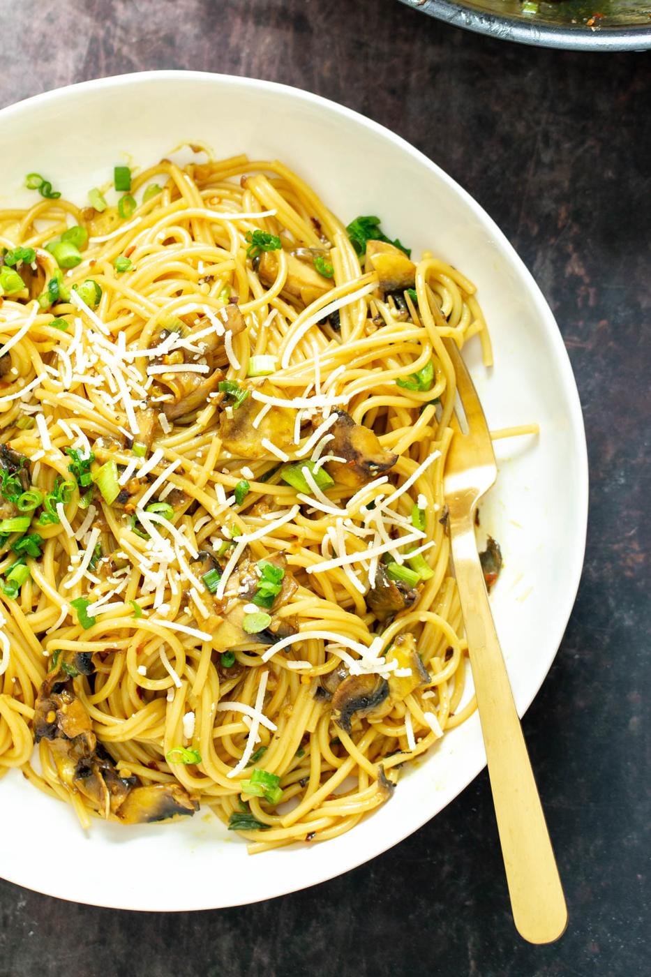 a plate of garlic pasta topped with grated parmesan and chopped scallions
