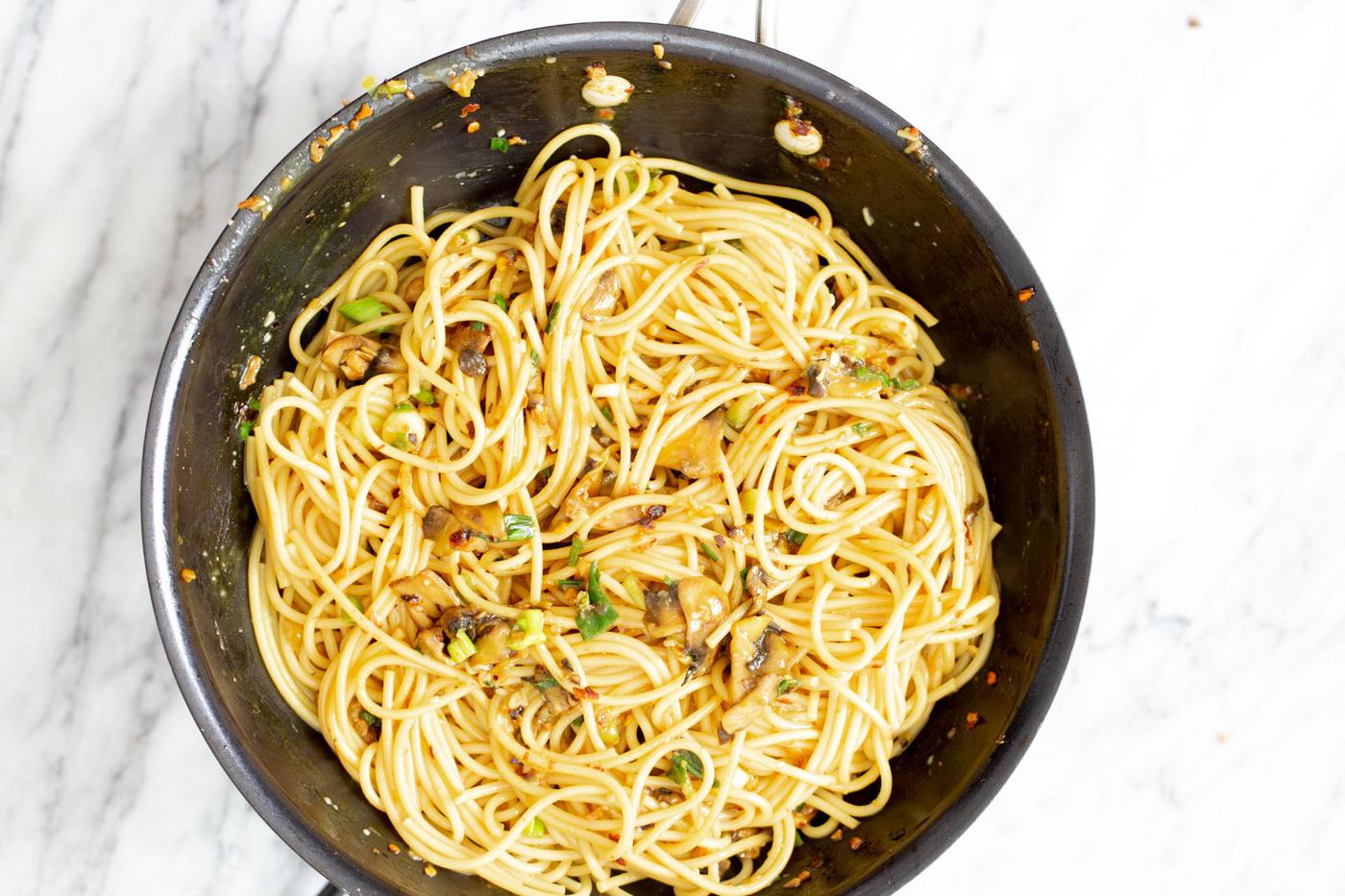 vegan garlic pasta being tossed with pasta water in a sauteeing pan