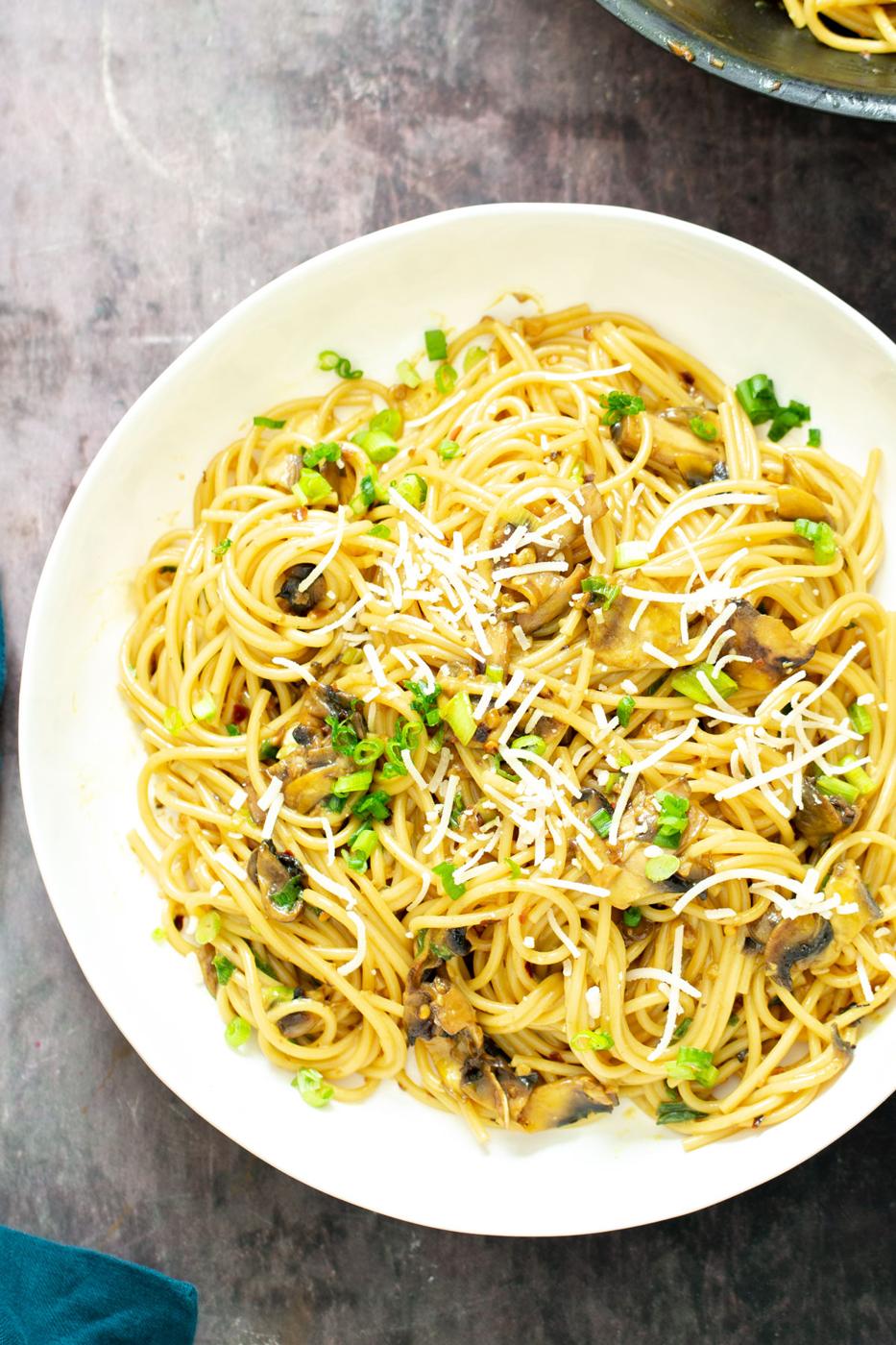 a plate with vegan garlic pasta with mushrooms topped with vegan parmesan and scallions