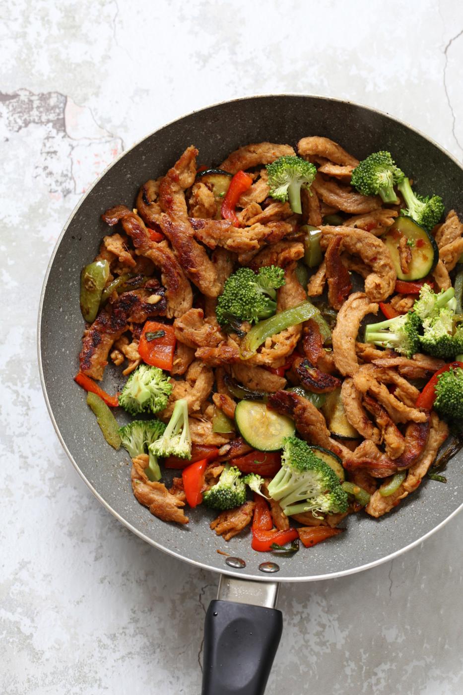 Vegegies and soy curls with general tsos sauce in grey skillet