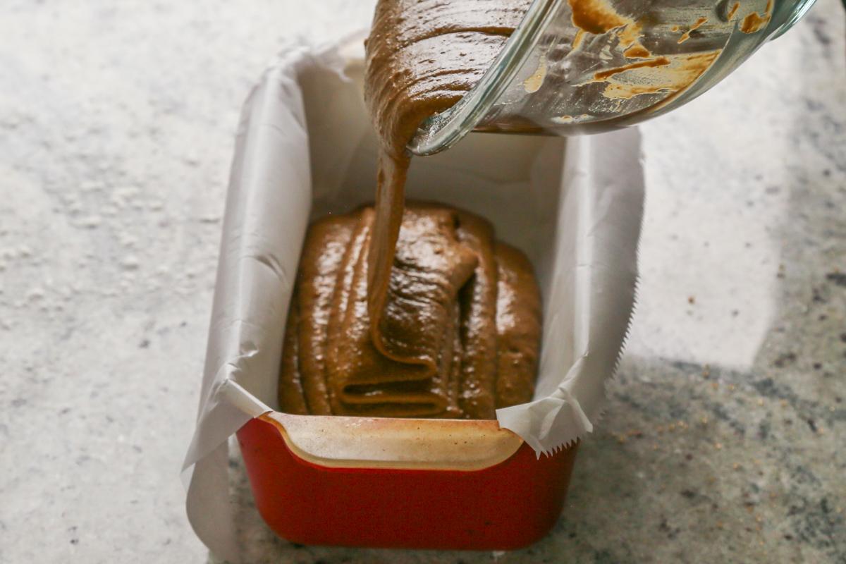 pouring gingerbread cake batter into a lined baking pan