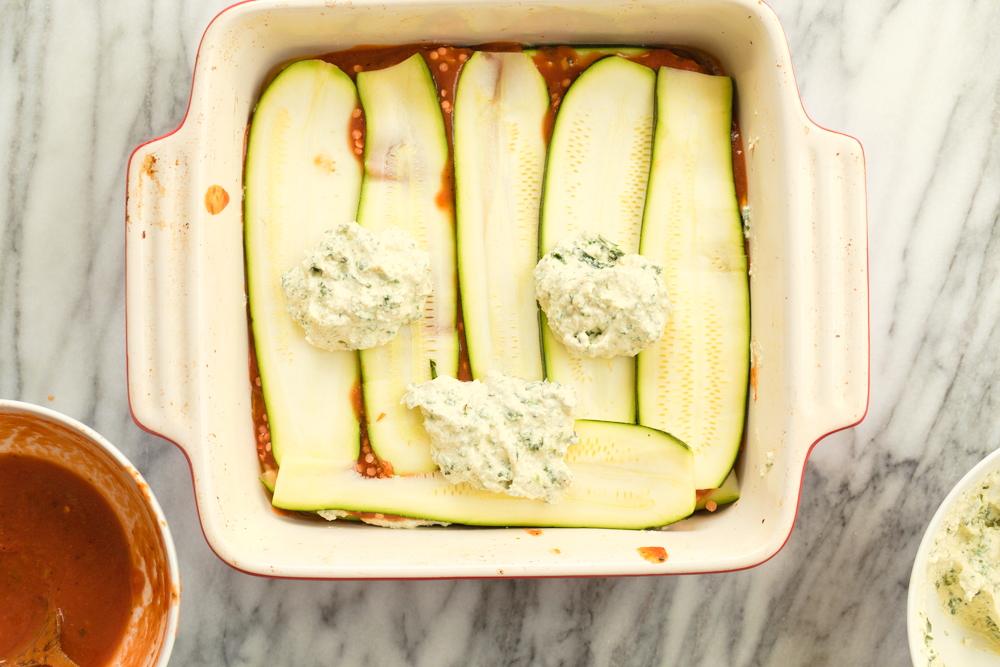Layering Our Vegan Gluten free Zucchini Lasagna in a cream baking dish