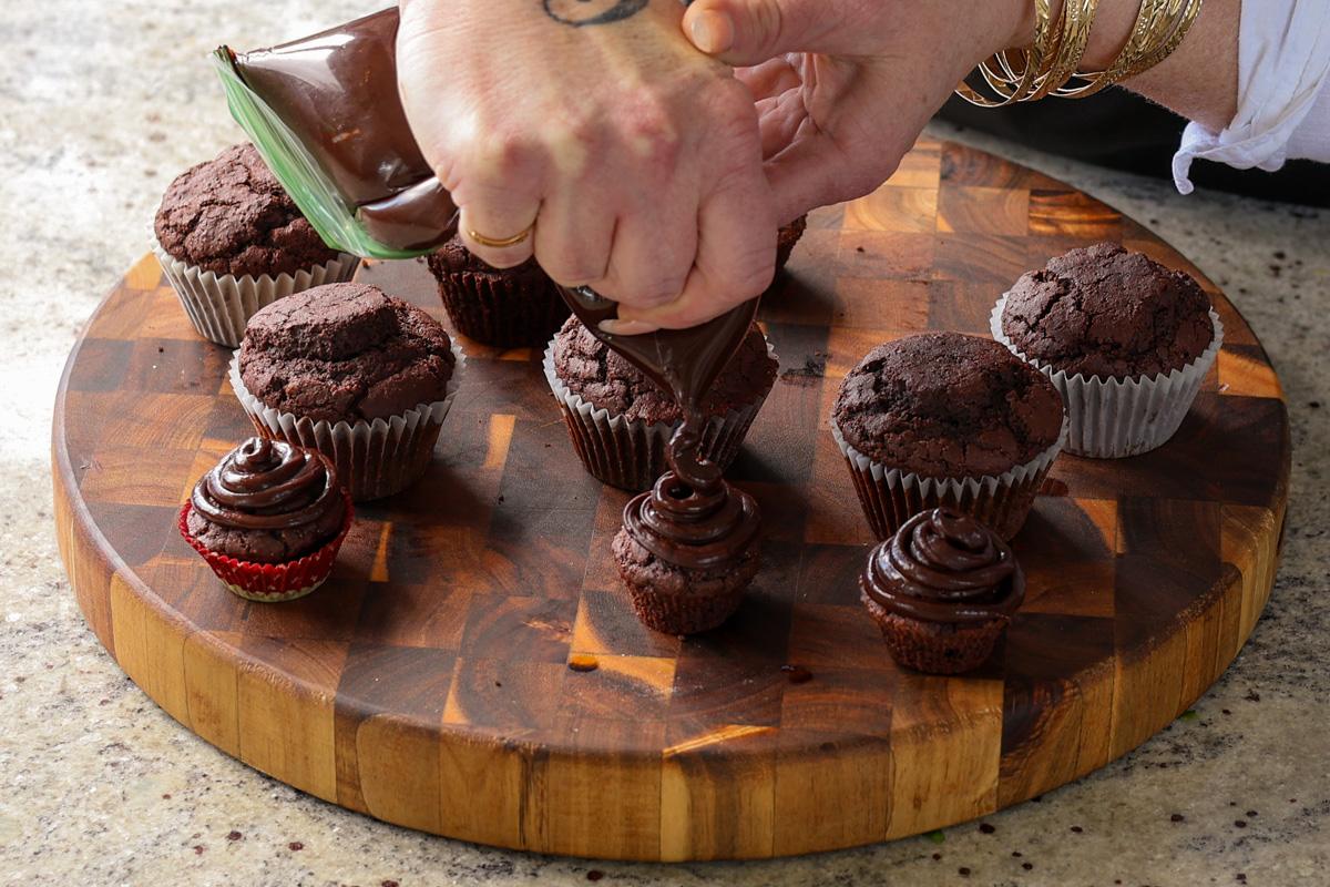 piping chocolate ganache frosting onto the gluten-free chocolate cupcakes
