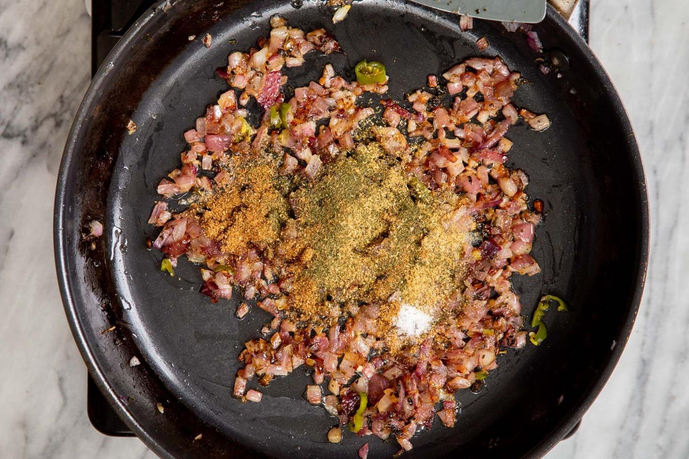 ground spices and minced onions in a black frying pan