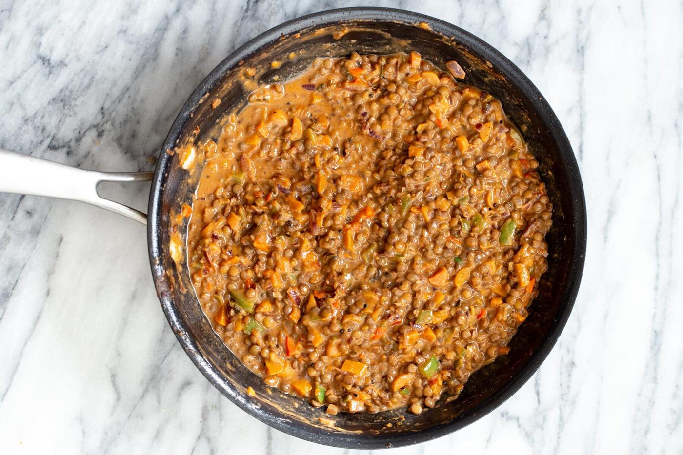cooked brown lentils simmering in creamy Indian gravy in black skillet